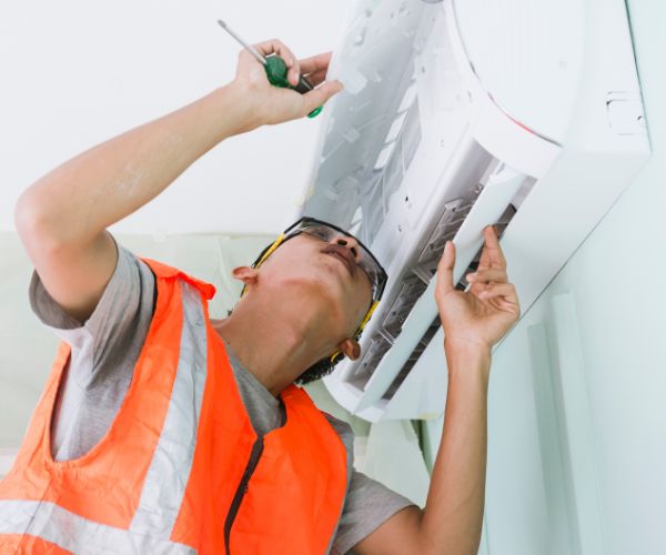 Technician repairing a wall-mounted air conditioner with a screwdriver