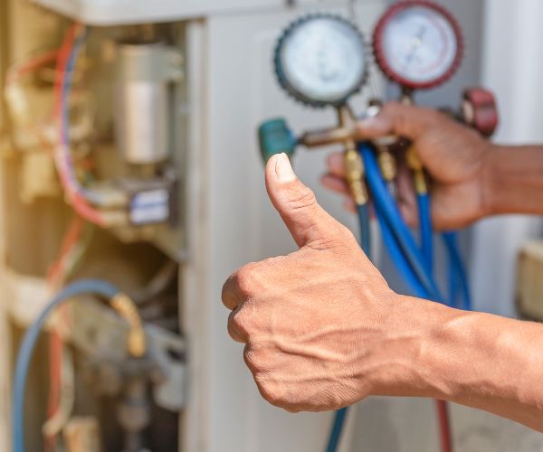 Technician checking AC refrigerant pressure with manifold gauges and giving a thumbs up